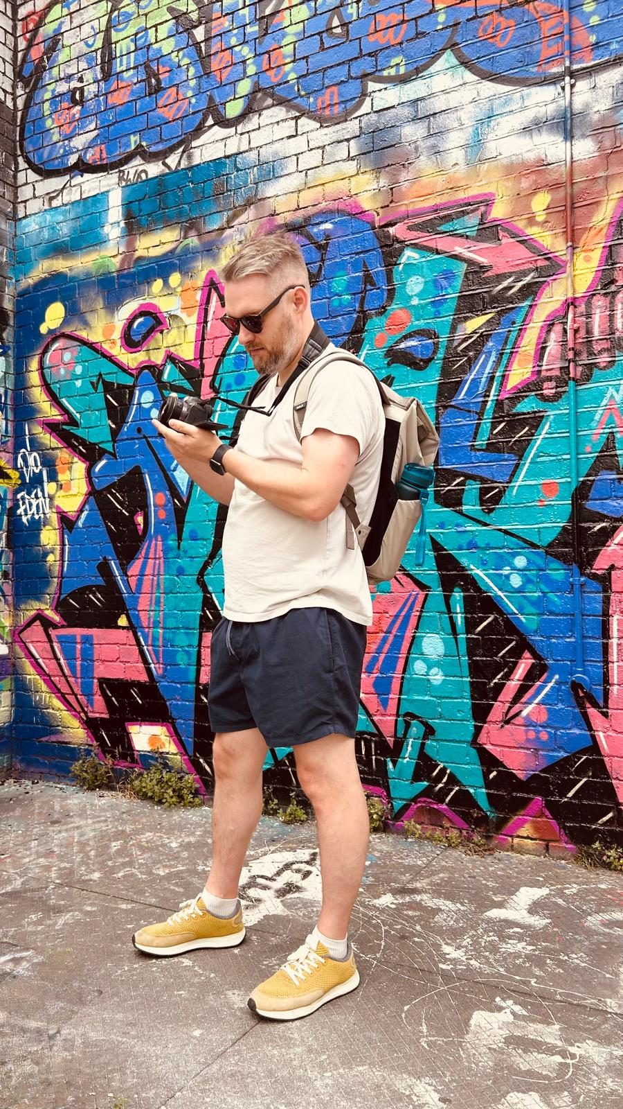Steven walking past a graffiti wall, checking the back of a camera.