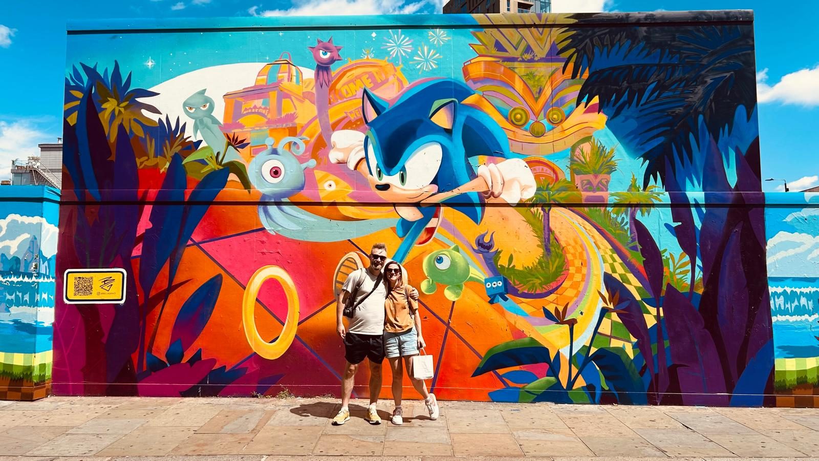 Steven and his partner standing in front of a large Sonic the Hedgehog street mural.