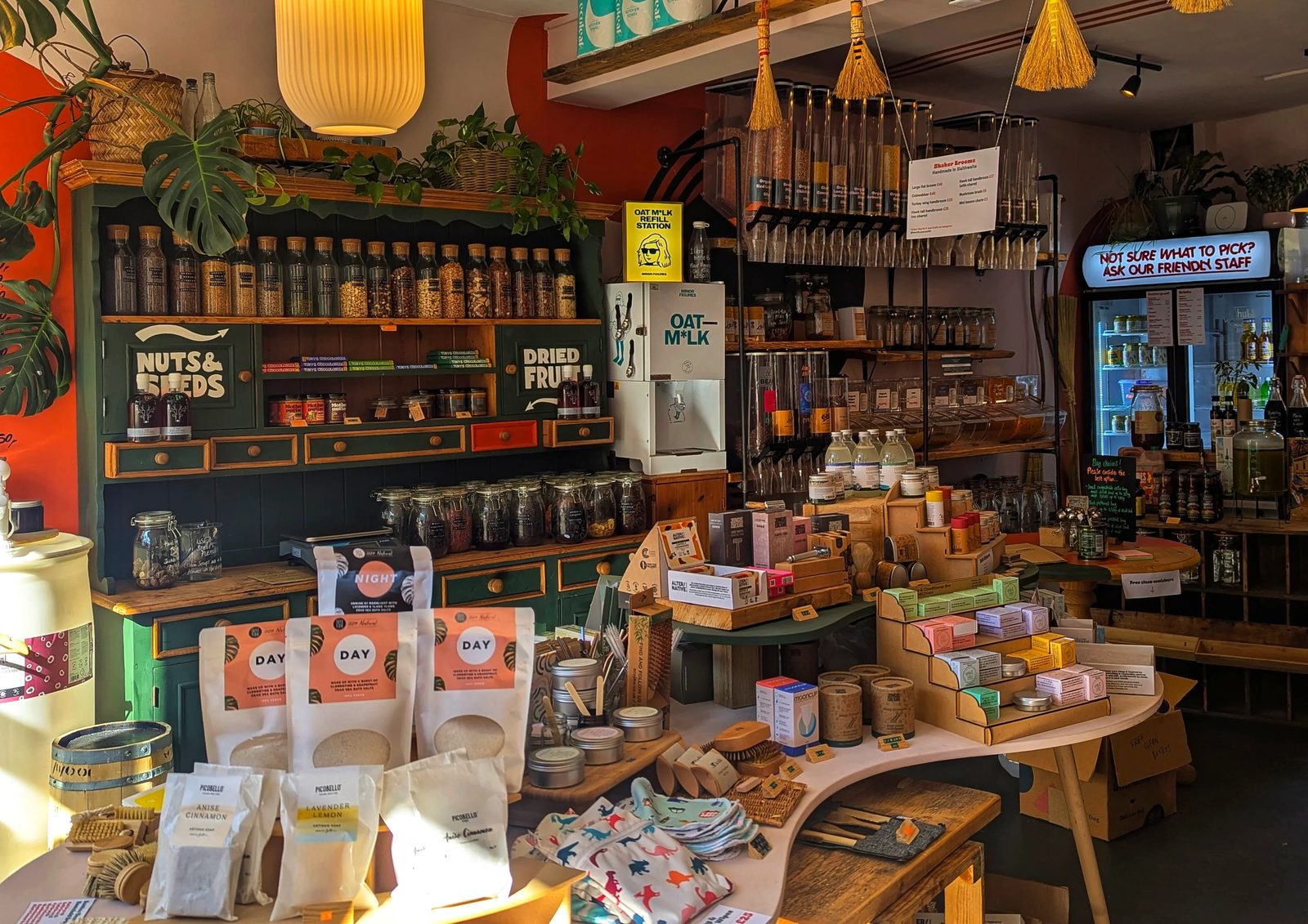 Inside a zero waste shop: shelves of labelled refill jars, an oat milk refill station, and tables of loose soaps, brushes and bath salts.